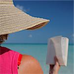Woman in sun hat reading on a tropical beach