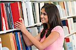 Female university student selecting book from library shelf