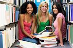 Three female students sitting on floor of library surrounded by books