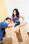 Young man sleeping while unpacking boxes, disapproving woman looking on