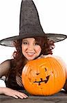 Portrait of Hispanic teenager girl in black Halloween hat and fishnet dress by stone fence with carved pumpkin (Jack O' Lantern) (focous on pumpkin)
