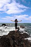 a beautiful woman doing yoga on the edge of the rocks with waves splashing to show a healthy way to live a happy and relaxed lifestyle in a world full of stress