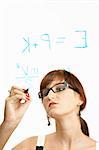 The young scientific girl in glasses with concentration writes formulas on glass