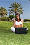 Young beautiful woman sitting on grass and using laptop
