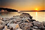 Image of a sunset in the town of Pylos, southern Greece, with rocks in the foreground and the island of Sfaktiria in the background