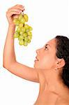 A woman looks on the bunch of grapes in her hands, standing on white background.