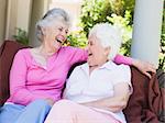 Senior female friends laughing together sitting on garden seat