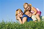 Smiling woman and kids in a heap laying on the grass outdoors