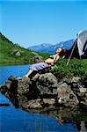 Young woman sunbathing on rocks next to lake