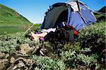 Camper relaxing at water's edge by tent