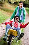 Son pushing laughing mother in wheelbarrow