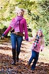 Mother and daughter running along path through autum woods