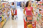 Two women pushing trolleys along supermarket aisle