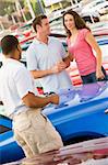 Couple discussing new car with salesman on lot