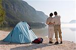 Couple standing beside a tent at a mountain lake on a misty morning