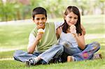 Two children eating ice cream in park looking to camera