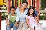 Mother and children in playground sitting on climbing frame