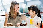 Mother and daughter eating cake and drinking juice in cafe