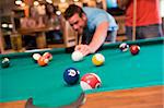 Young man playing pool in a bar (focus on pool table).