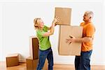 Middle-aged man holding cardboard moving boxes while woman places one on stack.