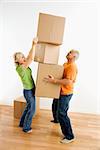 Middle-aged man holding stack of cardboard moving boxes while woman places another one on.