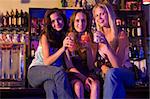 Three young women sitting on a bar counter, enjoying cocktails