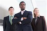 Three business people standing outdoors by building smiling