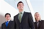 Three businesspeople standing outdoors by building smiling