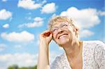 The elderly woman in glasses laughs against the sky