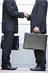 Two businessmen holding briefcases outdoors shaking hands