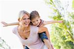 Woman giving young girl piggyback ride outdoors smiling