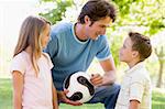 Man and two young children outdoors holding volleyball and smili
