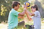 Man and young boy outdoors holding soccer ball and smiling