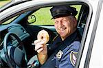 Police officer in his squad car holding a doughnut.
