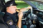 Police officer snacking on a donut while sitting in his squad car.