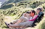Couple on cliffside outdoors using binoculars and smiling