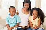 Woman and two children sitting in living room reading book and s