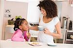 Woman and young girl in kitchen with cookies and coffee smiling