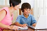 Woman helping young boy with laptop do homework in dining room s