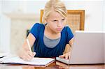 Young girl with laptop doing homework in dining room