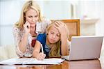 Woman helping young girl with laptop do homework in dining room