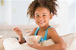 Young girl eating cereal in living room smiling.