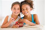 Two young girls eating strawberries in living room smiling