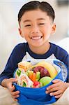 Young boy indoors with packed lunch smiling