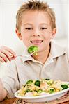 Young boy indoors eating pasta with brocolli smiling