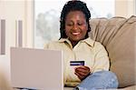 Woman in living room using laptop holding credit card and smilin