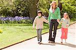 Mother and two young children walking on path holding hands smil