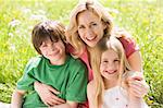 Mother and two young children sitting outdoors smiling