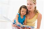 Mother and daughter indoors reading book and smiling