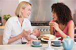 Mother and baby in kitchen with friend eating cake and smiling